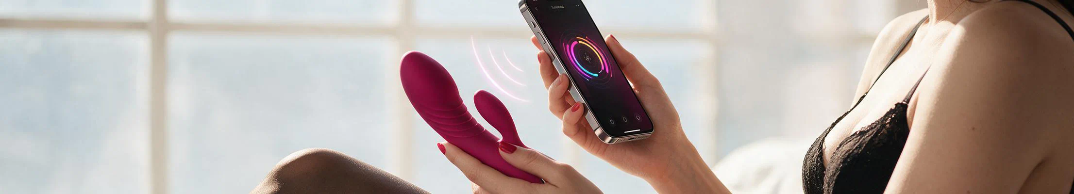 En kvinde i sort undertøj holder et app-styret sexlegetøj i den ene hånd og en smartphone i den anden.