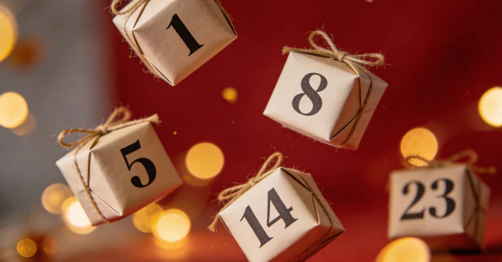 Adventskalendertal på små gaveæsker foran en stemningsfuld julebaggrund med lys – stemningsbillede til en Erotisk julekalender 2026.
