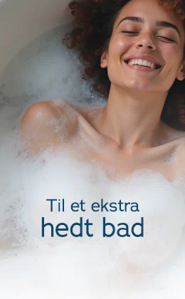 En smilende kvinde med krøllet brunt hår ligger afslappet i et hvidt badekar fyldt med skum. Der står med store bogstaver: "Til et ekstra hedt bad". Nederst viser en rød knap teksten "Find vandtætte legetøj »".